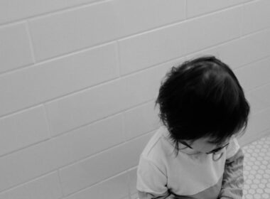 grayscale photo of child in white long sleeve shirt sitting on floor